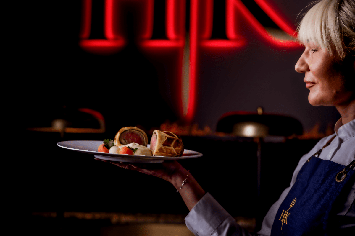 Fine Dining for Business Travellers Blog Image chef carrying a plate of food in front of the Kell's Kitchen sign